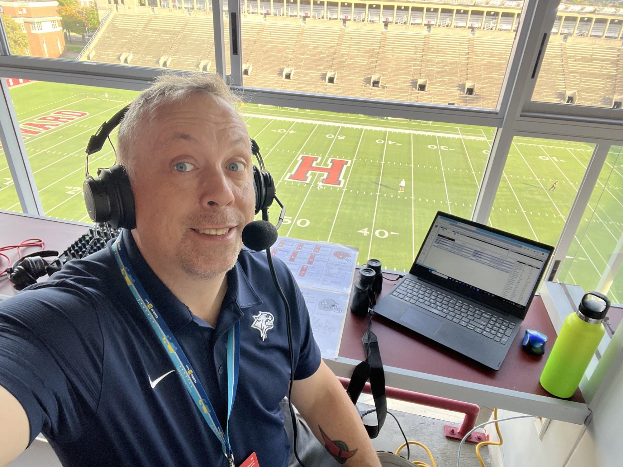 Justin McIsaac wearing a broadcast headset in a stadium press box